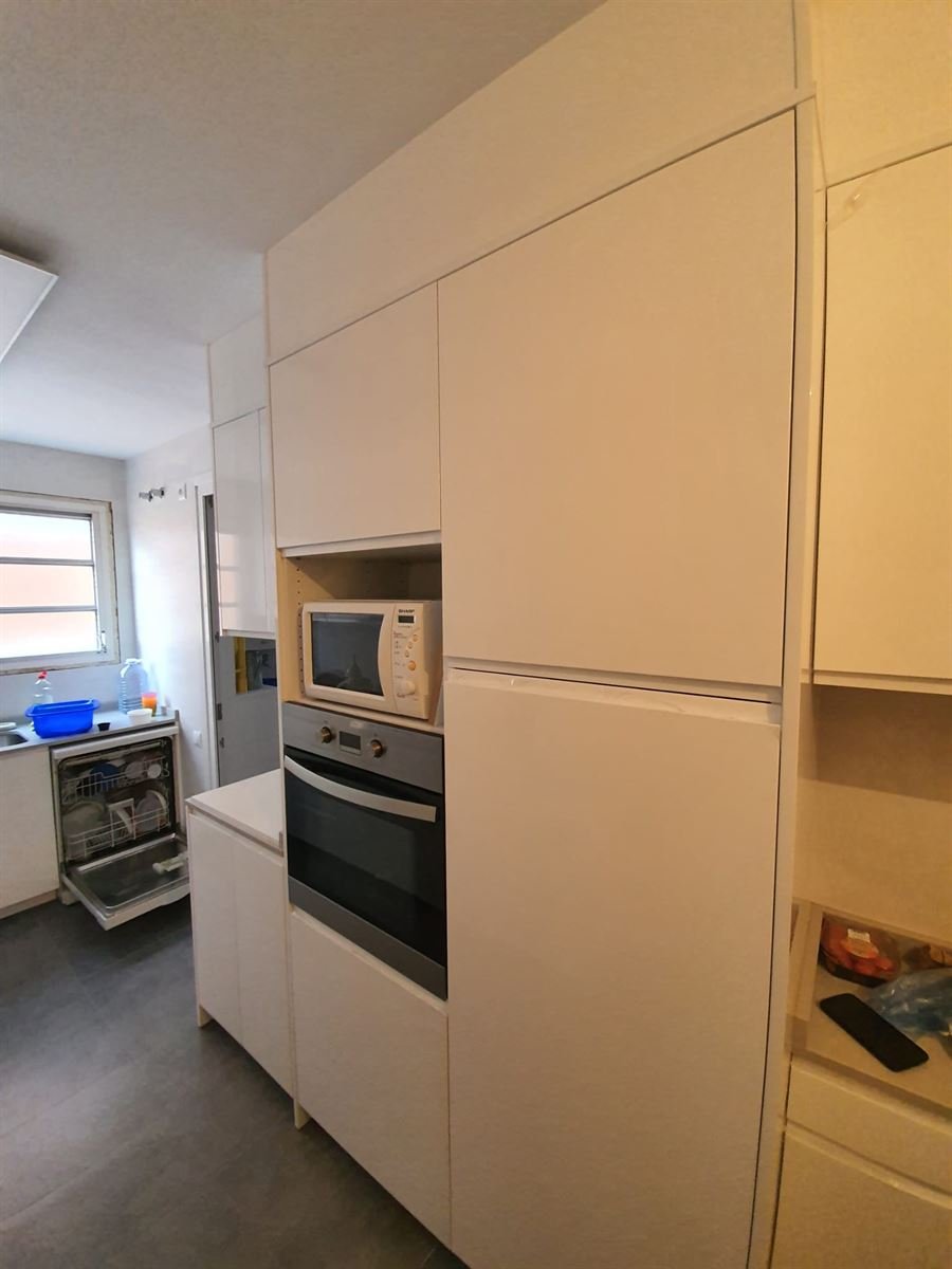 Cocina terminada con el mobiliario blanco sin tiradores, la columna de horno y microondas y el pavimento nuevo