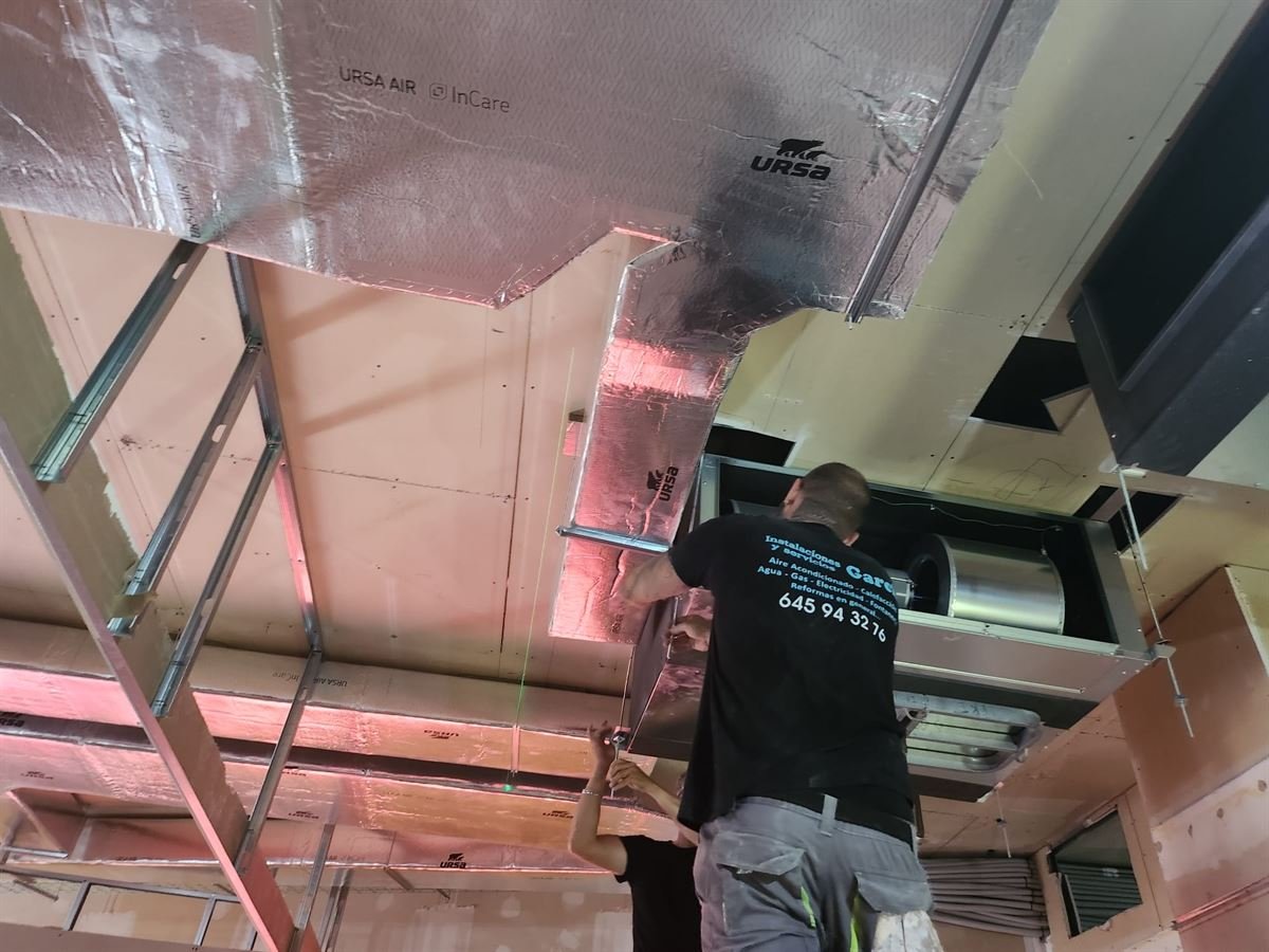 Técnico instalando los tramos de conducto aislado con fibra sobre la estructura del falso techo