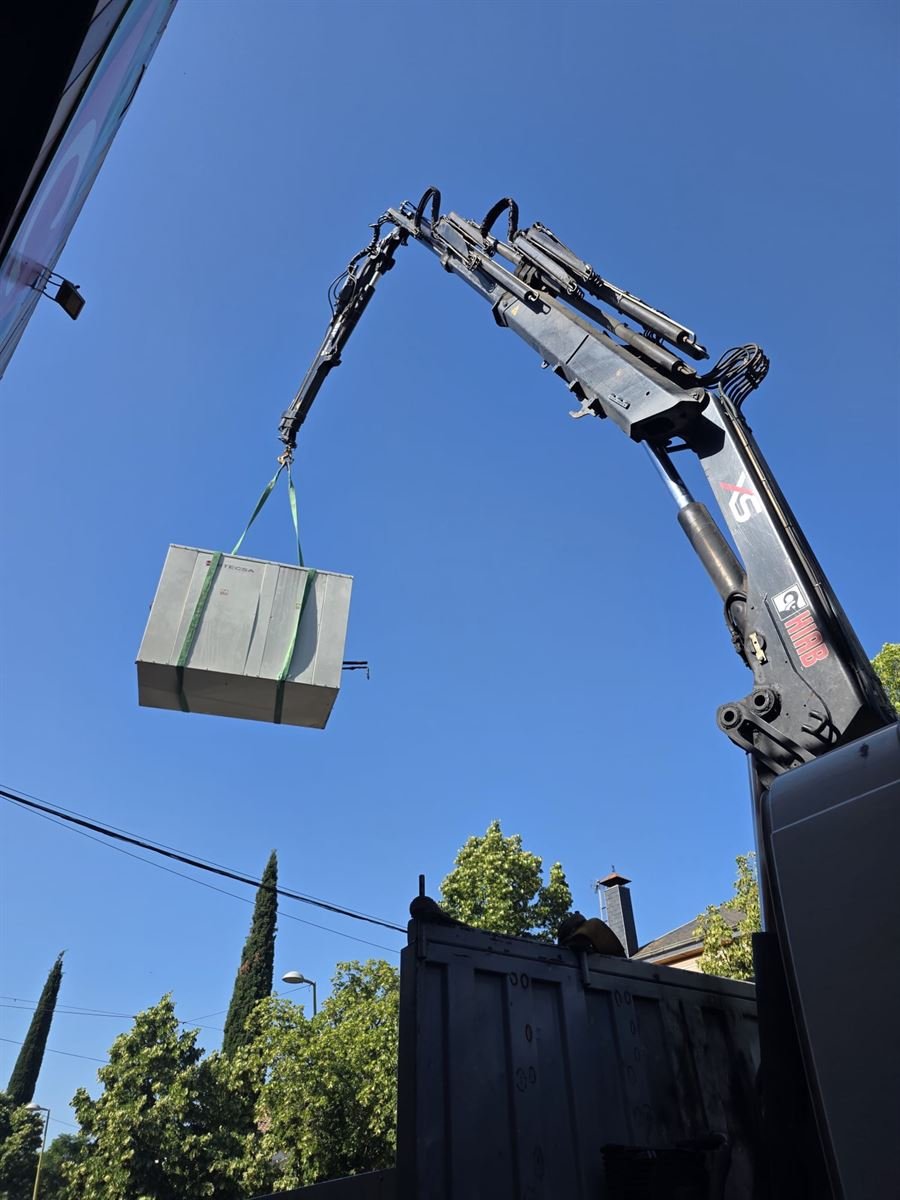 Grúa elevando una de las máquinas de climatización por encima del edificio del mercado