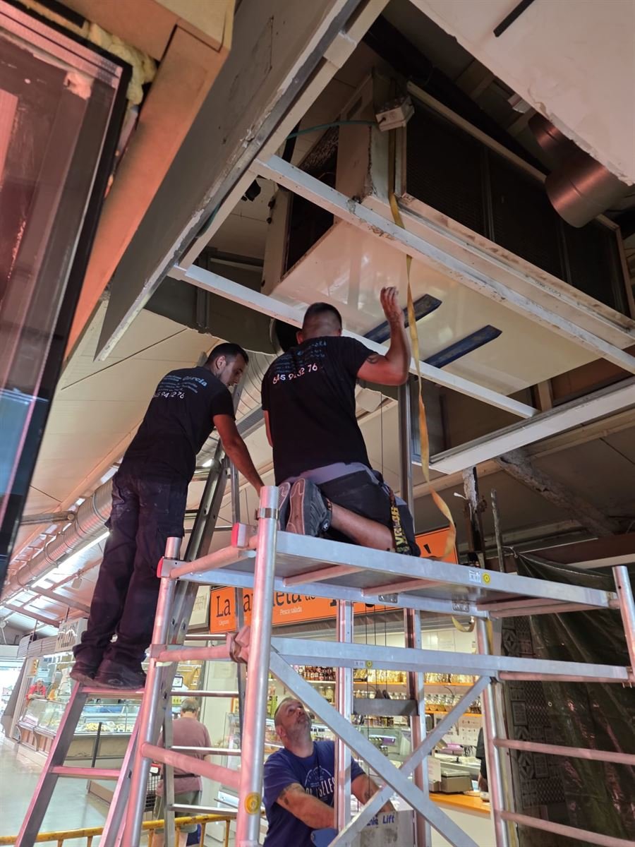 Dos técnicos de Instalaciones y Servicios JGDR trabajando desde el andamio sobre las paradas del mercado