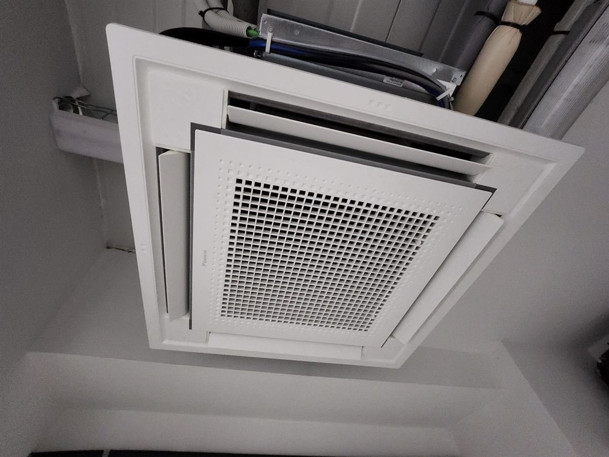 Unidad interior de cassette Daikin montada en el falso techo, con las tuberías y el cableado a la vista antes de cerrar
