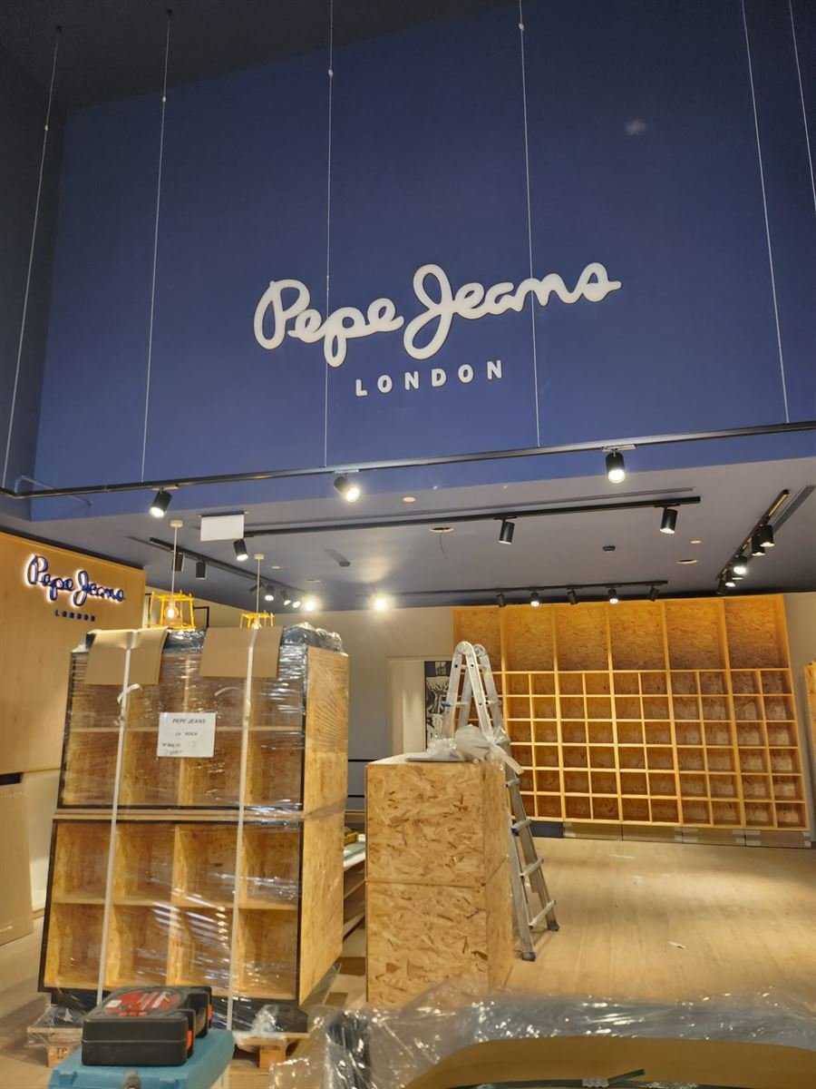 Interior de la tienda de Pepe Jeans en La Roca Village durante el montaje, con el rótulo iluminado y la iluminación de carril ya instalada