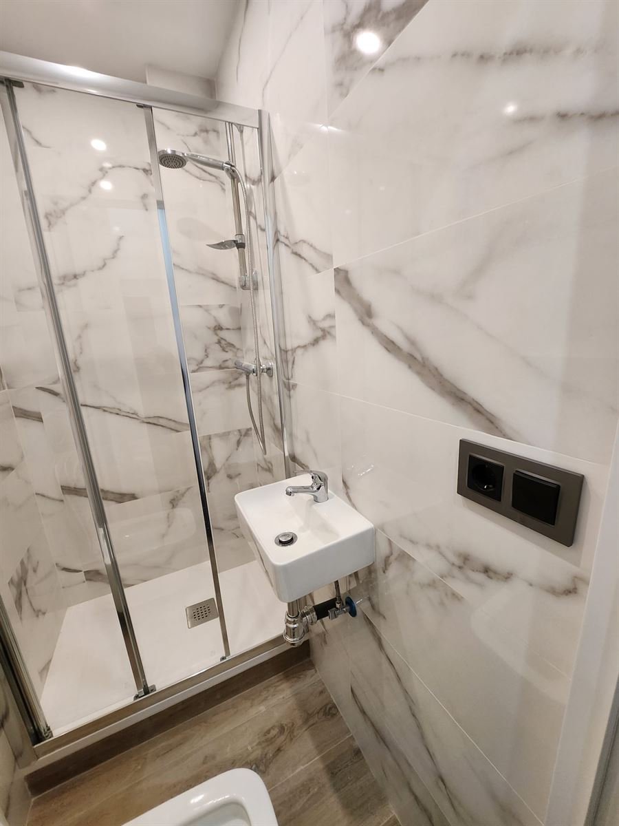 Baño acabado con el gran formato imitando mármol, la mampara de ducha y el lavabo suspendido