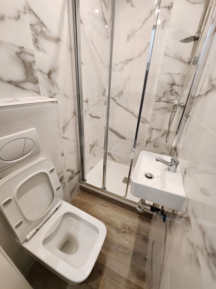 El baño terminado visto desde la puerta, con el inodoro suspendido, el lavabo y la ducha